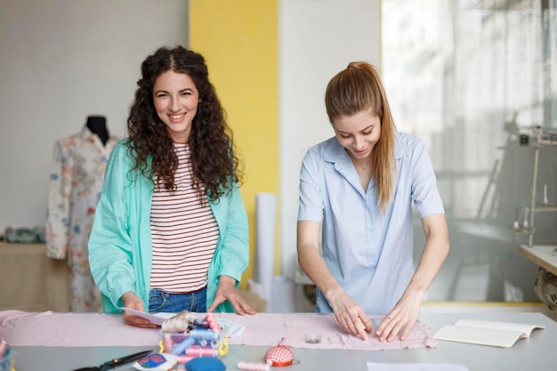 Bellissimi giovani designer che lavorano felicemente insieme a nuovi tessuti nel moderno laboratorio di cucito