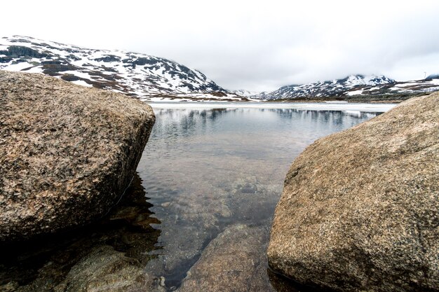 Bellissimo colpo di rocce lungo il fiume e la montagna innevata in Norvegia