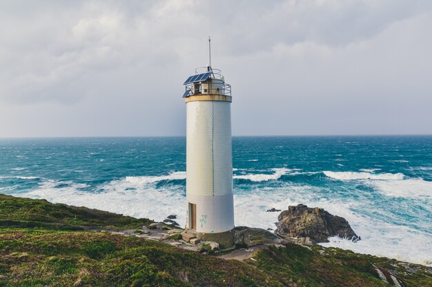 Bellissimo faro tra le scogliere con il magnifico mare in tempesta