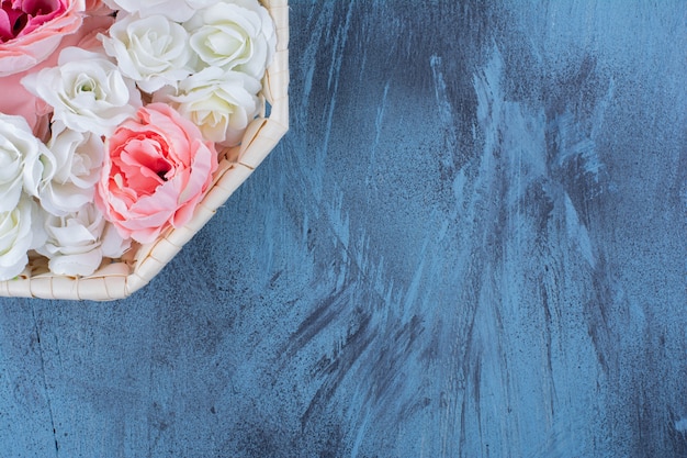 Bellissimo fiore di rosa colorato in cesto di vimini sull'azzurro.