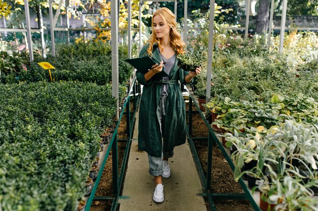 Bellissimo giardino botanico, pieno di molti fiori e cespugli verdi. Ragazza con capelli ricci biondi, pose, presentandosi come biologa.