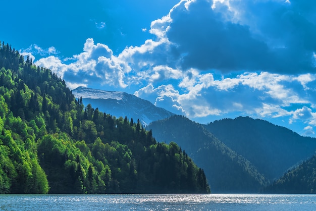 Bellissimo lago Ritsa nelle montagne del Caucaso. Colline verdi della montagna, cielo blu con le nuvole. Paesaggio primaverile.