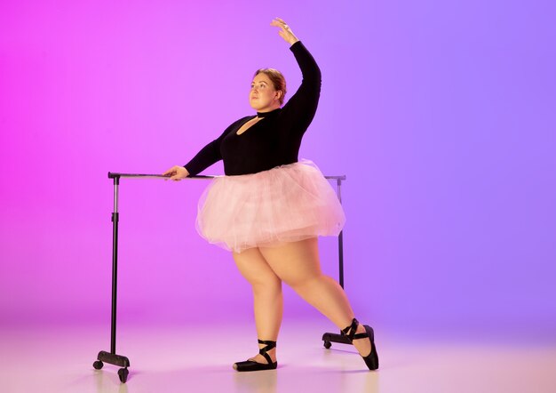 Bellissimo modello caucasico plus size che pratica danza classica su sfondo sfumato viola-rosa studio in luce al neon. Concetto di motivazione, inclusione, sogni e risultati. Vale la pena essere ballerina.