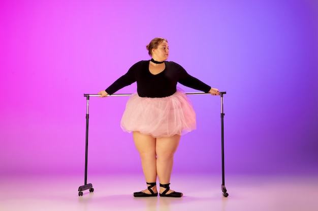 Bellissimo modello caucasico plus size che pratica danza classica su sfondo sfumato viola-rosa studio in luce al neon. Concetto di motivazione, inclusione, sogni e risultati. Vale la pena essere ballerina.