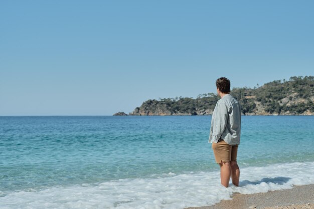 Bellissimo paesaggio estivo con un giovane in piedi tra le onde costiere e guardando il mare contro un cielo colorato e le isole viaggiano sullo sfondo Tempo libero e turismo stile di vita attivo