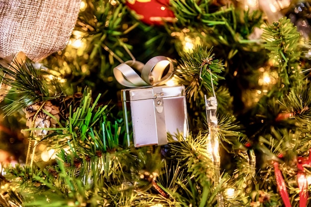 Bellissimo primo piano di un ornamento regalo d'argento e altre decorazioni su un albero di Natale con luci