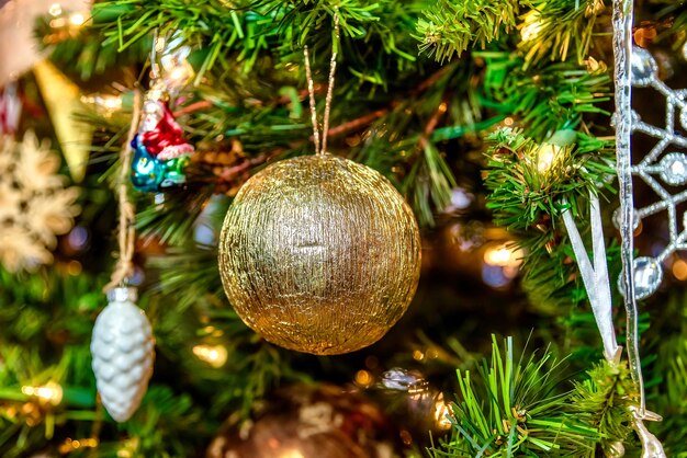 Bellissimo primo piano di una palla d'oro e altre decorazioni su un albero di Natale con luci