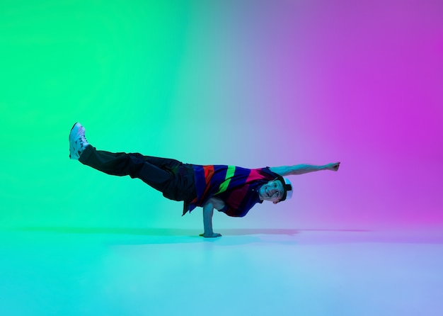 Bellissimo ragazzo sportivo che balla hip-hop in abiti eleganti sulla parete sfumata colorata nella sala da ballo alla luce al neon. Cultura giovanile, movimento, stile e moda, azione. Ritratto luminoso alla moda.