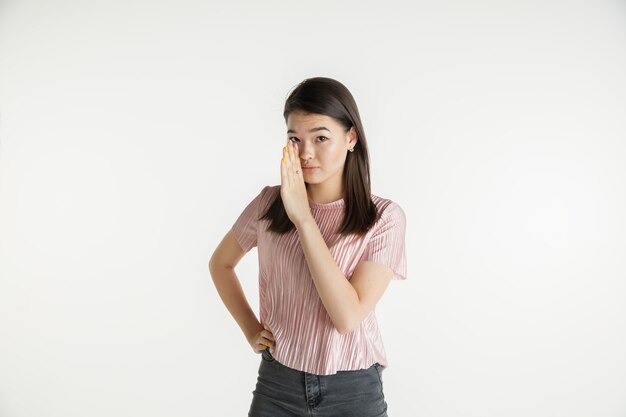 Bellissimo ritratto femminile a mezzo busto isolato su sfondo bianco studio. Giovane donna emotiva in abiti casual. Emozioni umane, concetto di espressione facciale. Sussurrando un segreto, vendite.