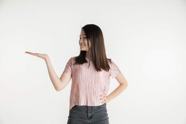 Bellissimo ritratto femminile a mezzo busto isolato su sfondo bianco studio. Giovane donna emotiva in abiti casual. Emozioni umane, concetto di espressione facciale. Tiene e mostra copyspace, sorride.