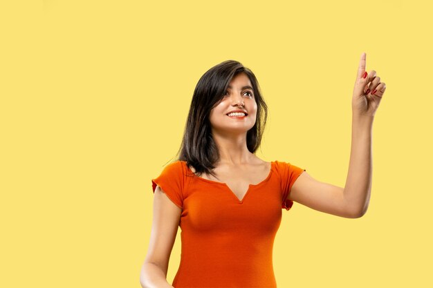 Bellissimo ritratto femminile a mezzo busto isolato su sfondo giallo studio. Giovane donna indiana emotiva in vestito che indica e che mostra. Spazio negativo. Espressione facciale, concetto di emozioni umane.