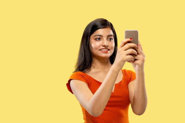 Bellissimo ritratto femminile a mezzo busto isolato su spazio giallo. Giovane donna indiana emotiva in abito che fa selfie. Spazio negativo