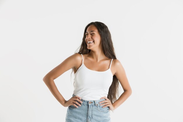 Bellissimo ritratto femminile a mezzo busto isolato sul muro bianco. Giovane donna afro-americana emotiva con i capelli lunghi. Espressione facciale, concetto di emozioni umane. In piedi e sorridente.