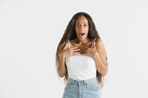 Bellissimo ritratto femminile a mezzo busto isolato sul muro bianco. Giovane donna afro-americana emotiva con i capelli lunghi. Espressione facciale, concetto di emozioni umane. Stupito, eccitato.