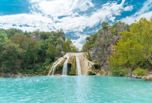 Bellissimo scatto di un lago con cascate sottili immerse nel verde e nelle montagne