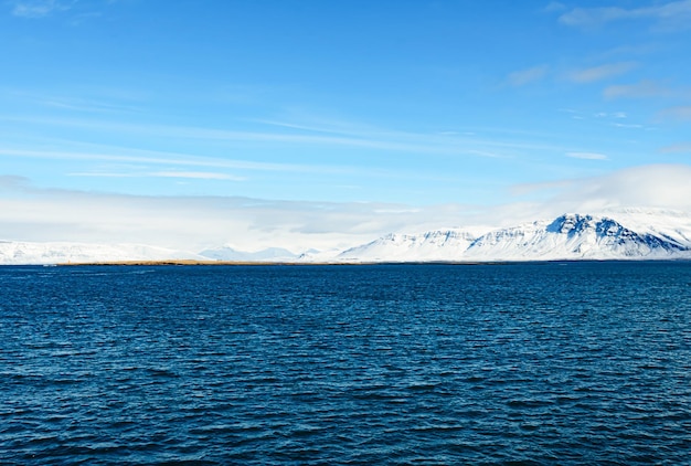 Bellissimo scatto di un mare blu pieno di onde davanti a una montagna innevata in Islanda