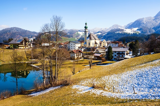 Bellissimo scatto di un piccolo villaggio circondato da un lago e colline innevate