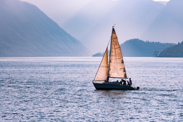 Bellissimo scatto di una barca a vela che attraversa il mare circondato dalle montagne