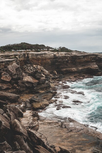 Bellissimo scatto verticale di una grande scogliera accanto all'acqua blu in una giornata uggiosa, perfetta per gli sfondi