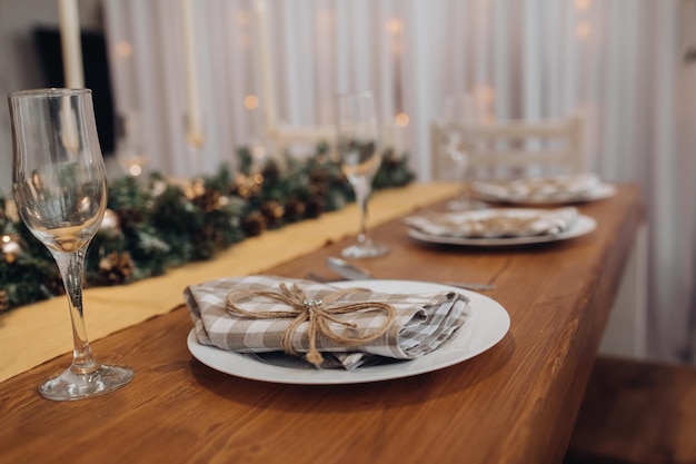 Bellissimo tavolo da portata natalizio con candele e decorazioni di abeti in un accogliente e moderno primo piano interno. Festeggiamo il capodanno delle vacanze di dicembre circondati da bicchieri e piatti decorati di stagione
