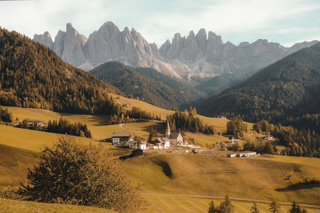 Bellissimo villaggio su una collina erbosa asciutta circondata dalle montagne boscose di giorno