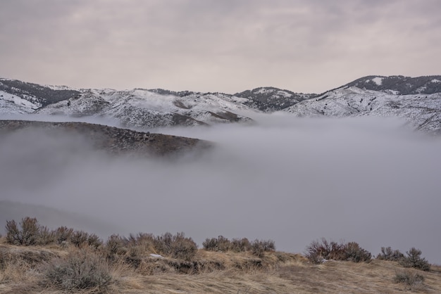 Bello colpo delle montagne nevose sopra la nebbia con un cielo nuvoloso