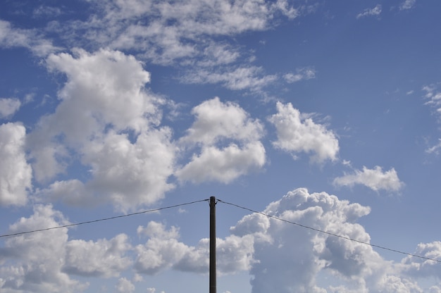 Bello colpo delle nuvole bianche nel cielo blu con un palo di elettricità nel mezzo