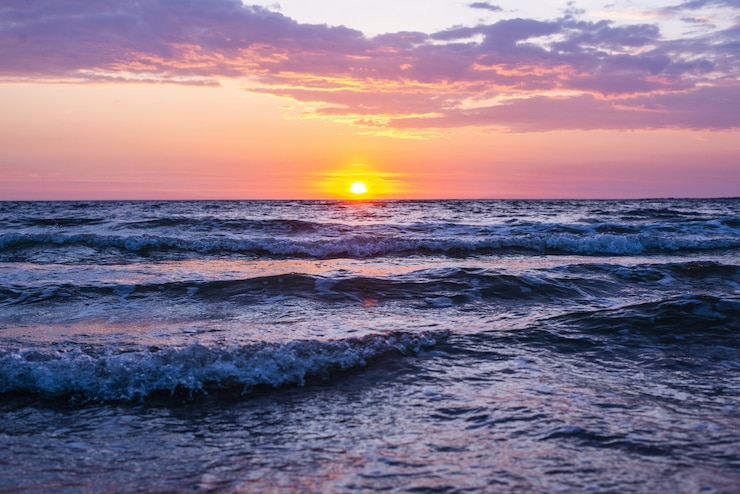 Foto gratuito bello colpo delle onde del mare sotto il cielo rosa e porpora con il sole che splende durante l'ora dorata