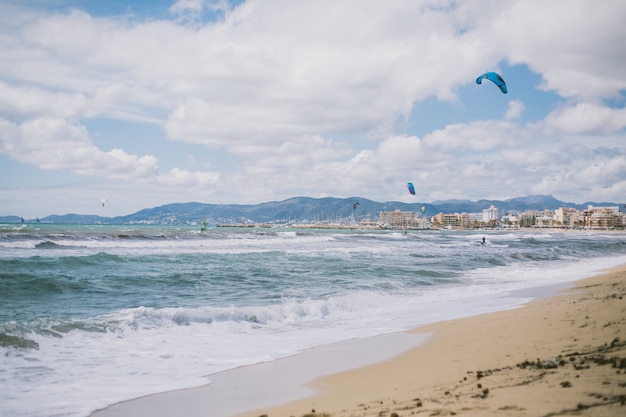 Bello colpo delle onde di oceano e degli aerostati sulla spiaggia sotto il cielo nuvoloso