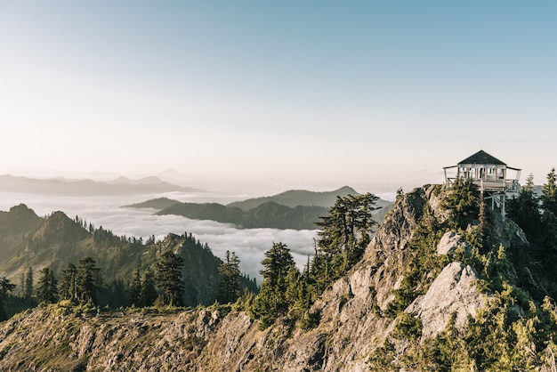 Bello colpo di un gazebo bianco in cima alla montagna vicino agli alberi con un cielo libero nel fondo