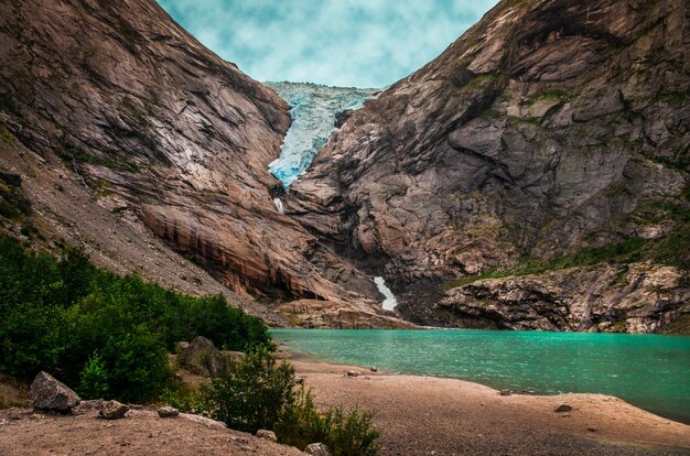 Bello colpo di un lago vicino alle alte montagne rocciose sotto il cielo nuvoloso in Norvegia