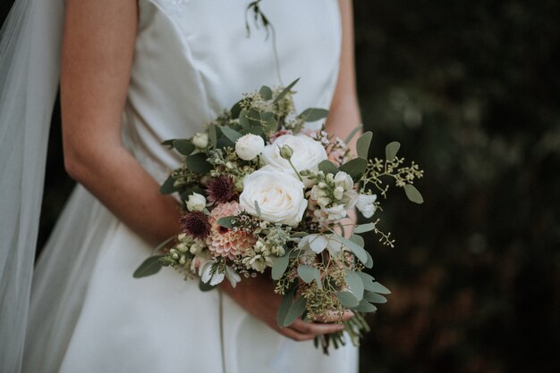 Bello colpo di un vestito da sposa d'uso da sposa che tiene un mazzo del fiore