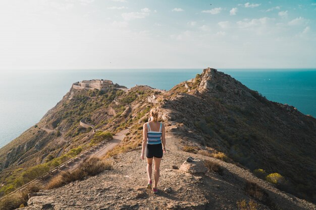 Bello colpo di una donna che cammina su una collina accanto all'oceano con il cielo soleggiato nei precedenti