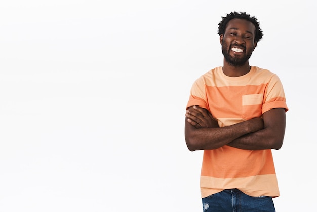 Bello e allegro giovane afroamericano con taglio di capelli afro, barba, mani incrociate sul petto, ridendo