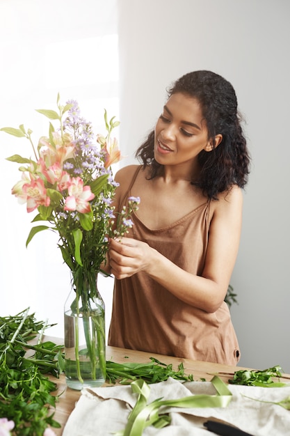 Bello fiorista femminile africano che sorride facendo mazzo di fiori.