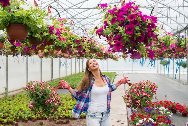 Bello fiorista femminile che tiene le piante da fiore in vaso in serra che si sente felice e positivo