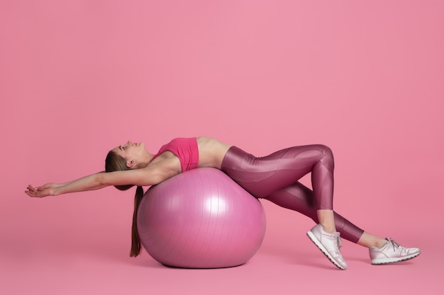 Bello giovane atleta femminile che si esercita sul ritratto monocromatico della parete rosa dello studio