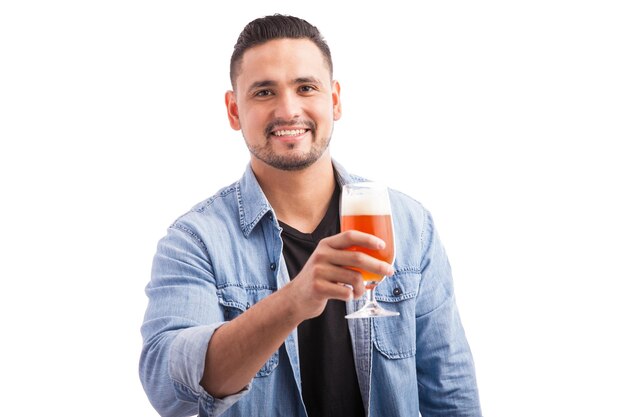 Bello giovane che beve birra da un bicchiere e sorride su uno sfondo bianco