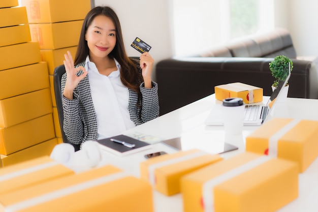 Bello giovane lavoro asiatico della donna del ritratto dalla casa con la carta di credito e la scatola di cartone pronte per la spedizione di acquisto