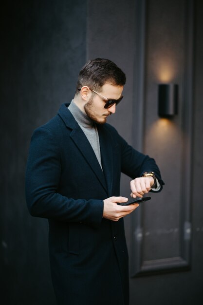 Bello giovane modello di moda in posa sulle strade della città. Ritratto di moda all'aperto, uomo elegante in cappotto elegante.