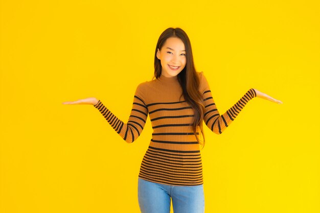 Bello giovane sorriso asiatico della donna adulta del ritratto con molta azione sulla parete gialla