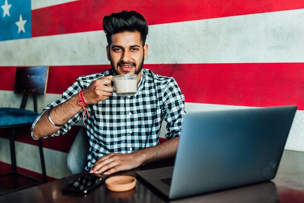 Bello, giovane uomo d'affari americano, libero professionista in abiti casual al bar, rilassante con una tazza di caffè.