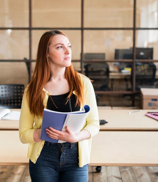 Bello libro e matita e pensiero della tenuta della donna graziosa