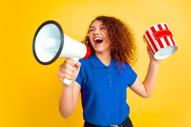 Bello modello riccio femminile in camicia con il megafono e il secchio dei popcorn