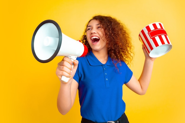 Bello modello riccio femminile in camicia con il megafono e il secchio dei popcorn