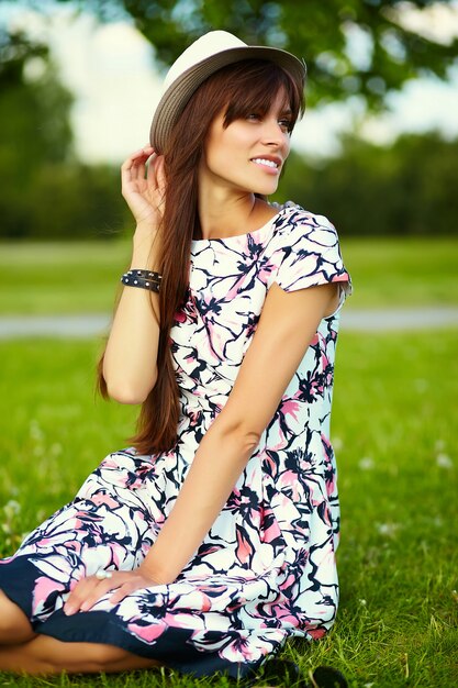 Bello modello sorridente alla moda divertente della giovane donna in vestito luminoso dal panno di estate in cappello nel parco
