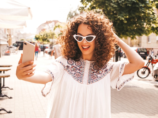 Bello modello sorridente con l'acconciatura di riccioli afro vestito in abito bianco hipster estate.