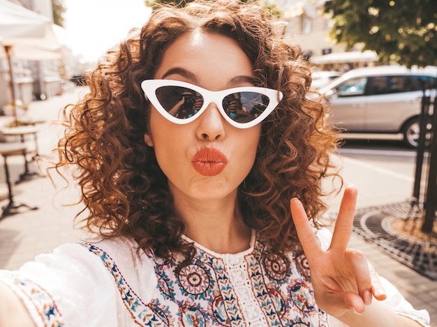 Bello modello sorridente con l'acconciatura di riccioli afro vestito in abito bianco hipster estate.