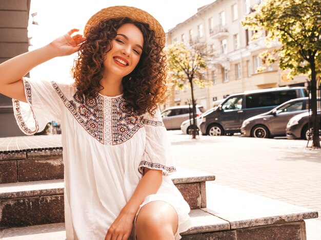 Bello modello sorridente con l'acconciatura di riccioli afro vestito in abito bianco hipster estate.