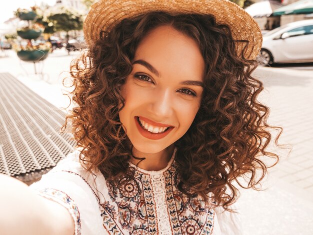 Bello modello sorridente con l'acconciatura di riccioli afro vestito in abito bianco hipster estate.